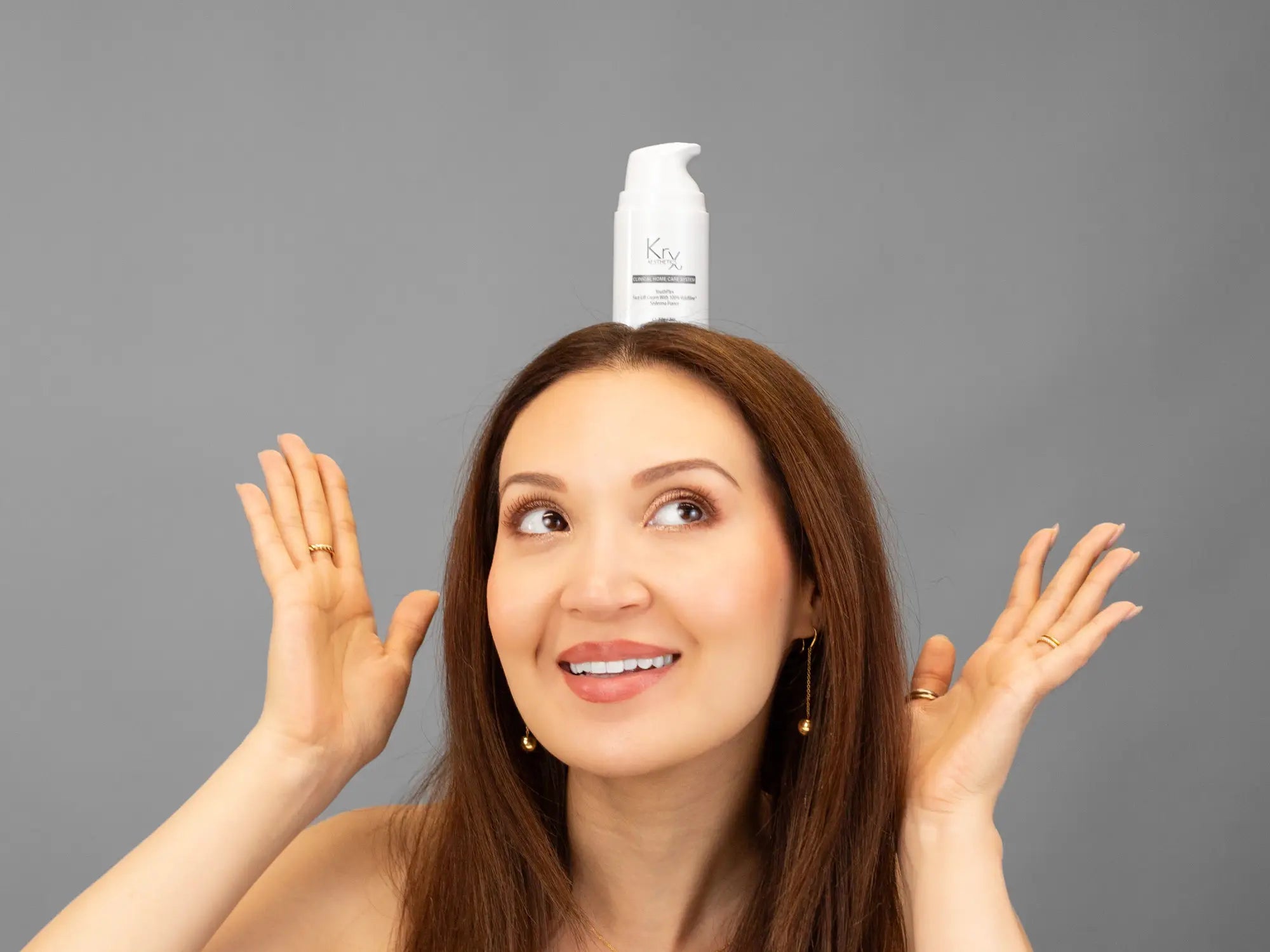 Laziza from LAZ Skincare holding a bottle of KrX Aesthetics Youthplex Face Lift Cream up to her face