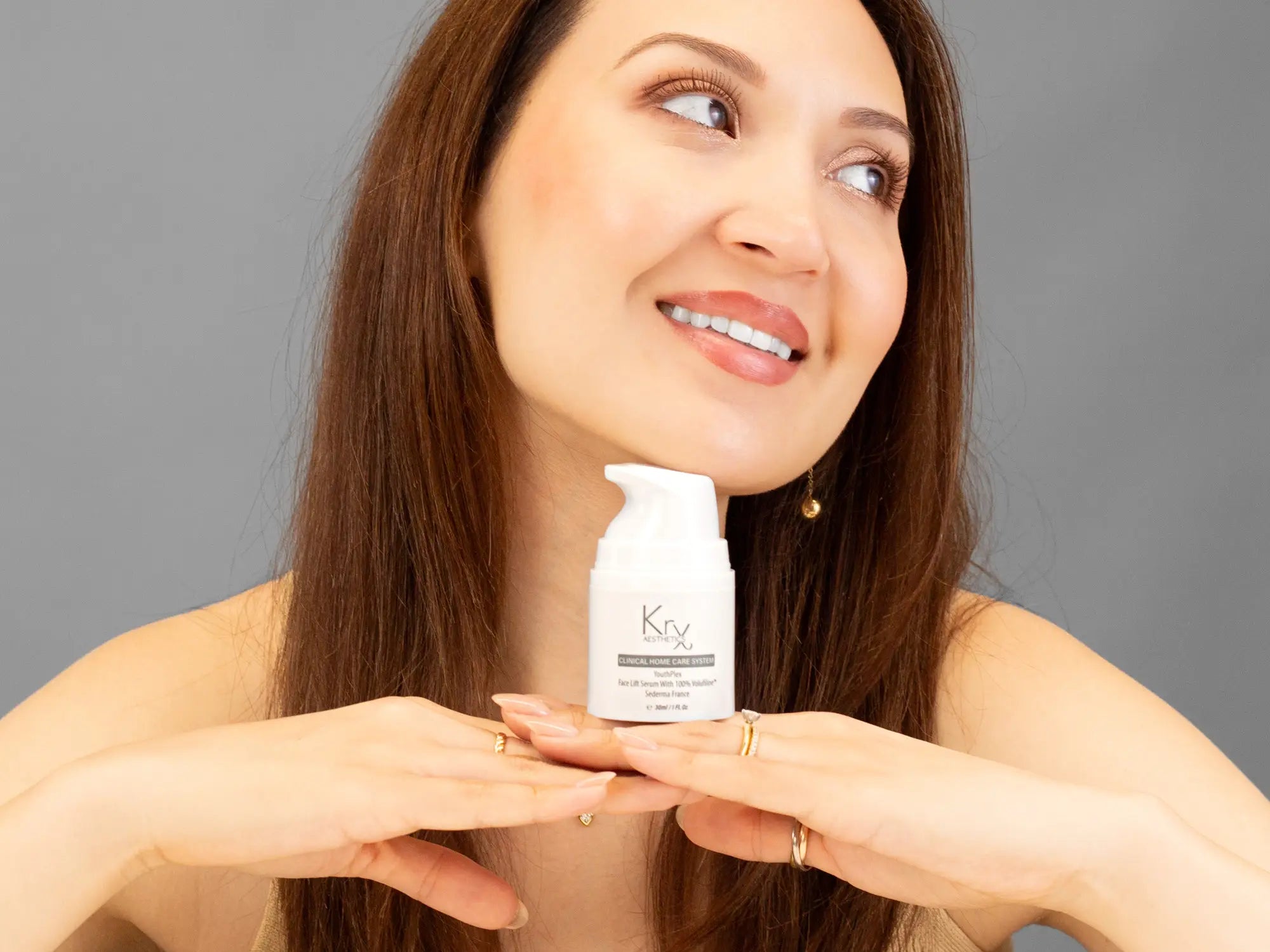 Laziza from LAZ Skincare holding a bottle of KrX Aesthetics Youthplex Face Lift Serum up to her face