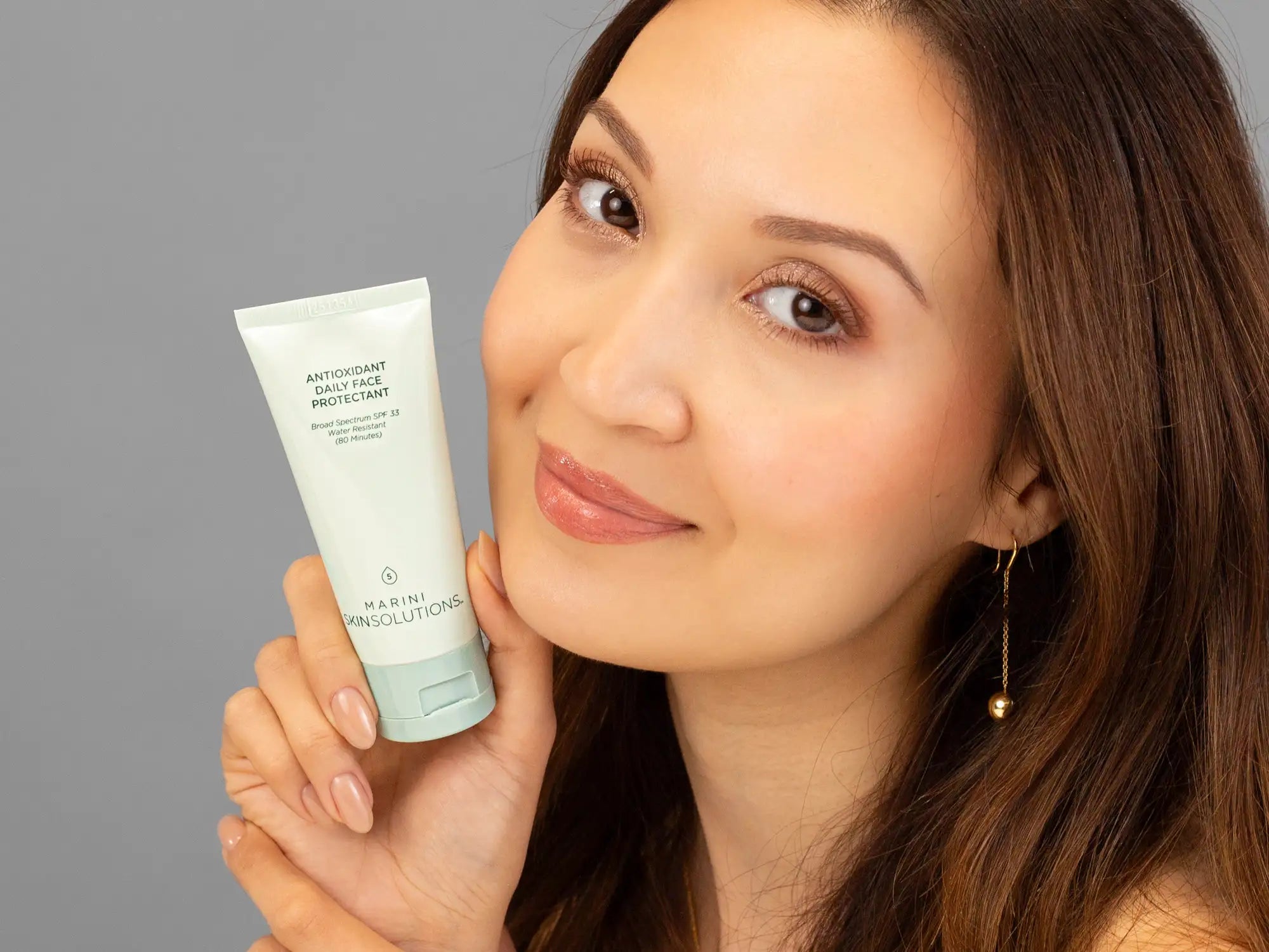 Laziza from LAZ Skincare holding a bottle of Marini SkinSolutions Antioxidant Daily Face Protectant SPF 33 up to her face