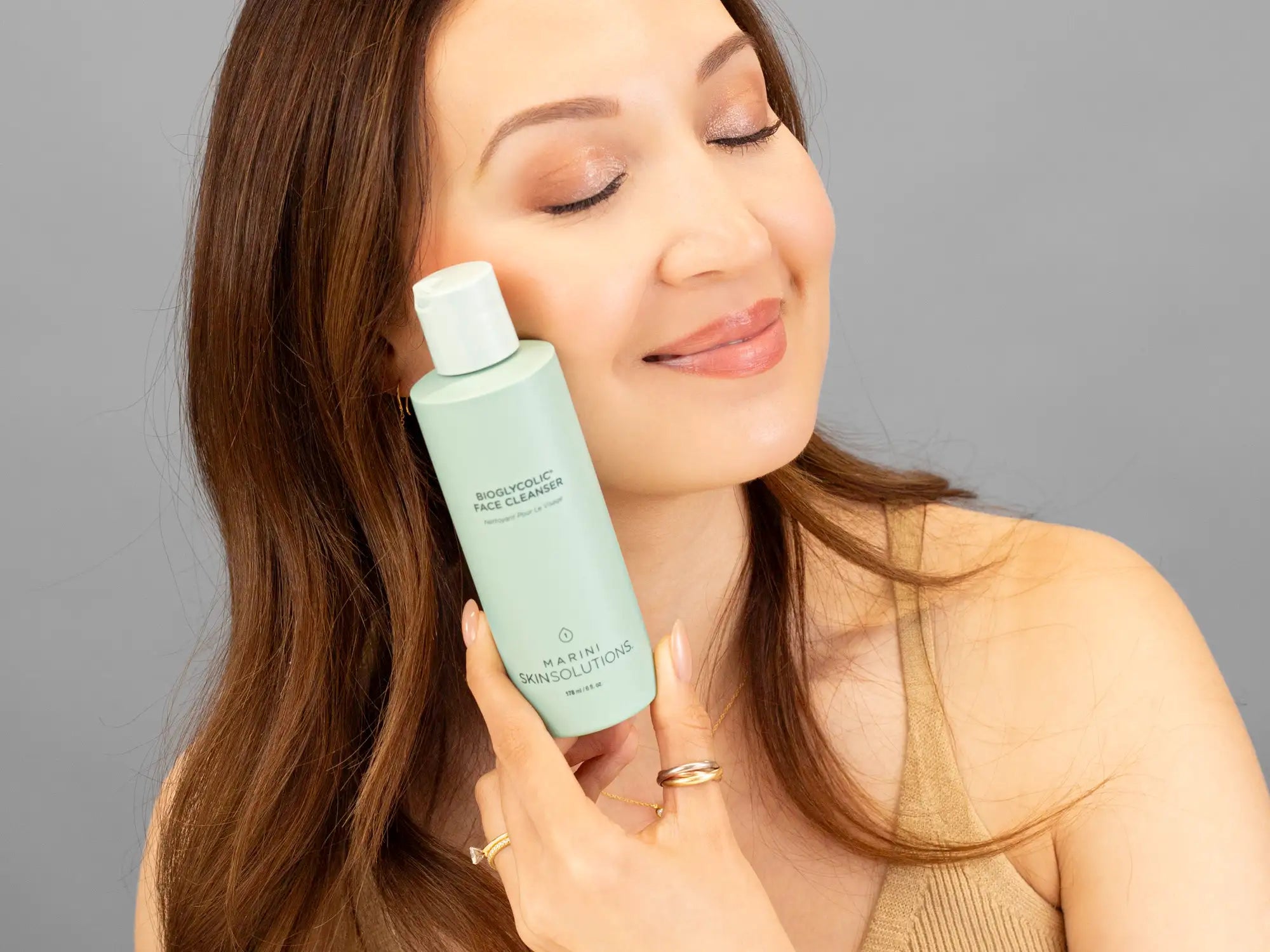 Laziza from LAZ Skincare holding a bottle of Marini SkinSolutions Bioglycolic Face Cleanser up to her face