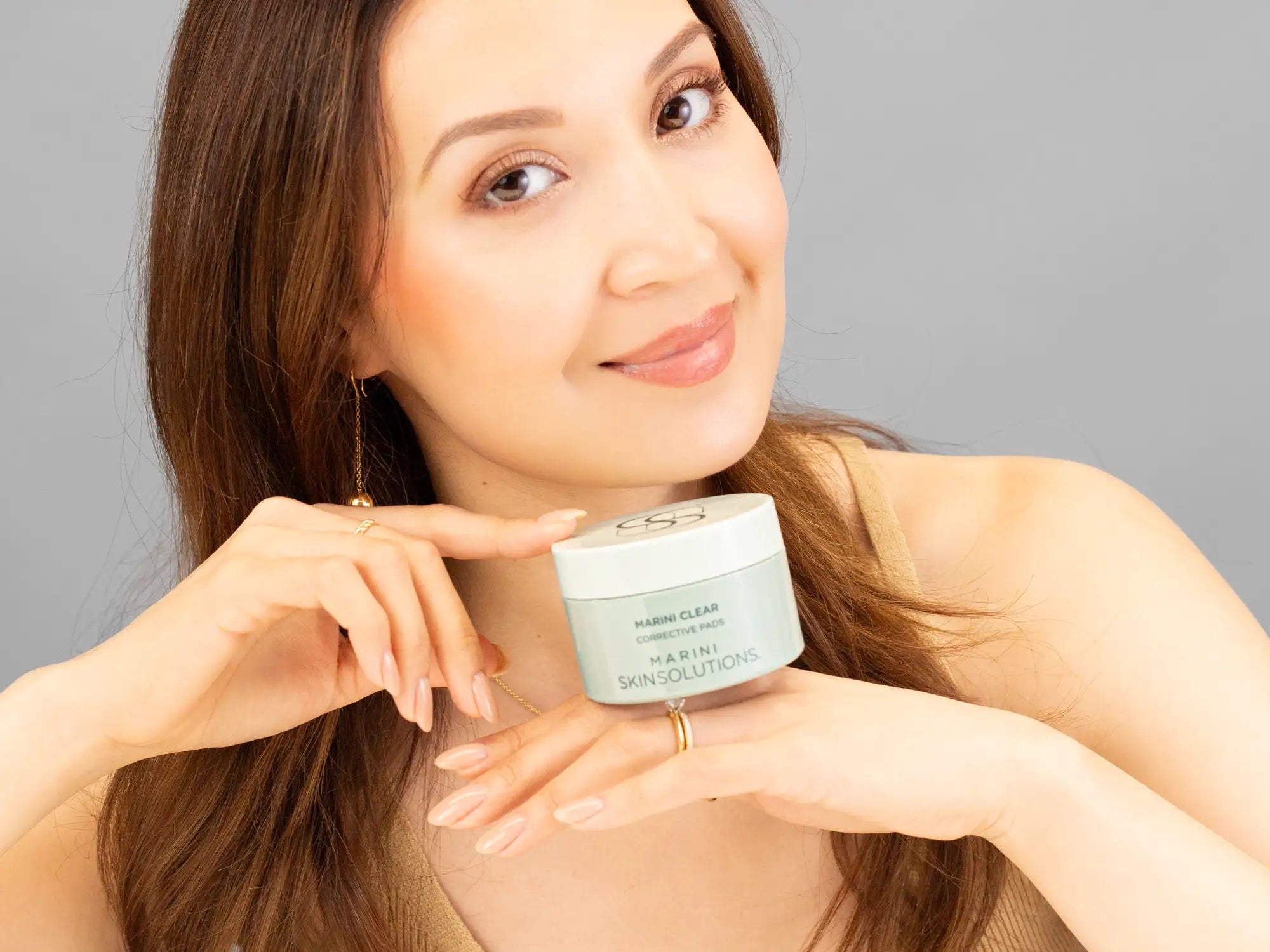 Laziza from LAZ Skincare holding a bottle of Marini SkinSolutions Marini Clear Corrective Pads up to her face