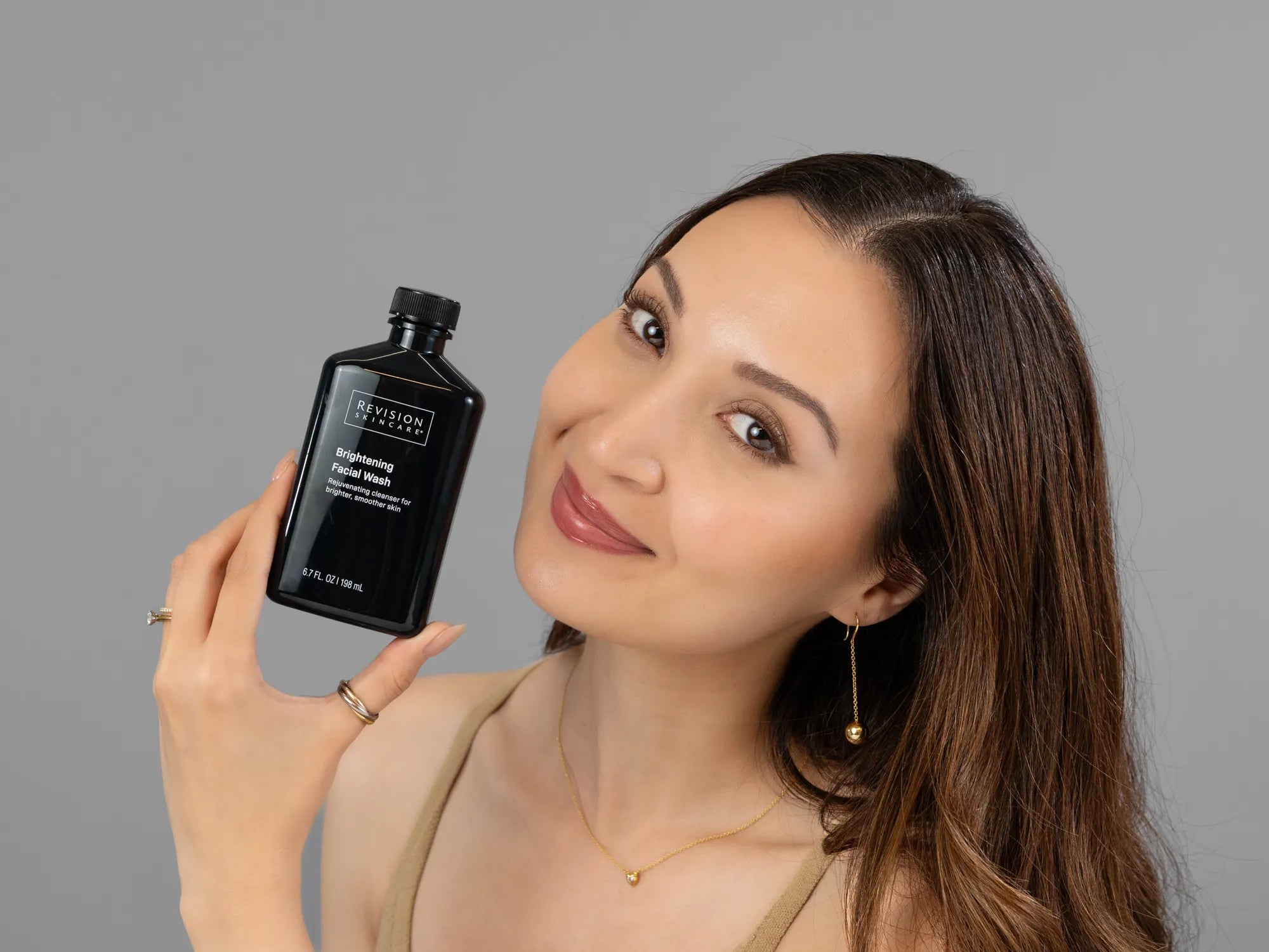 Laziza from LAZ Skincare holding a bottle of Revision Brightening Facial Wash up to her face