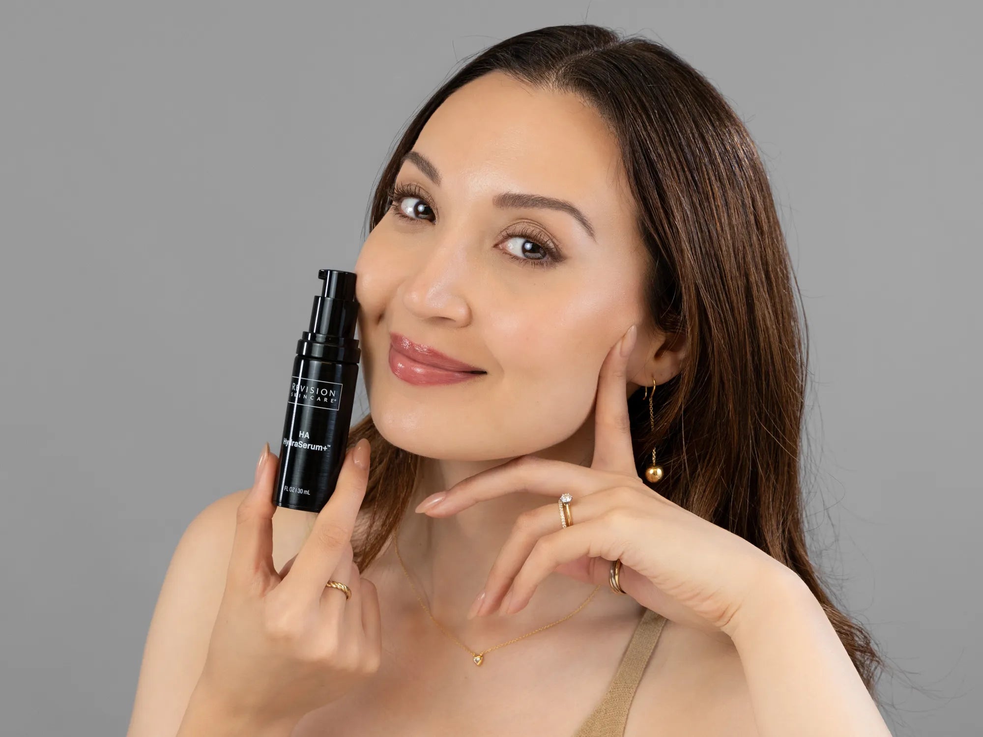 Laziza from LAZ Skincare holding a bottle of Revision HA HydraSerum+ up to her face