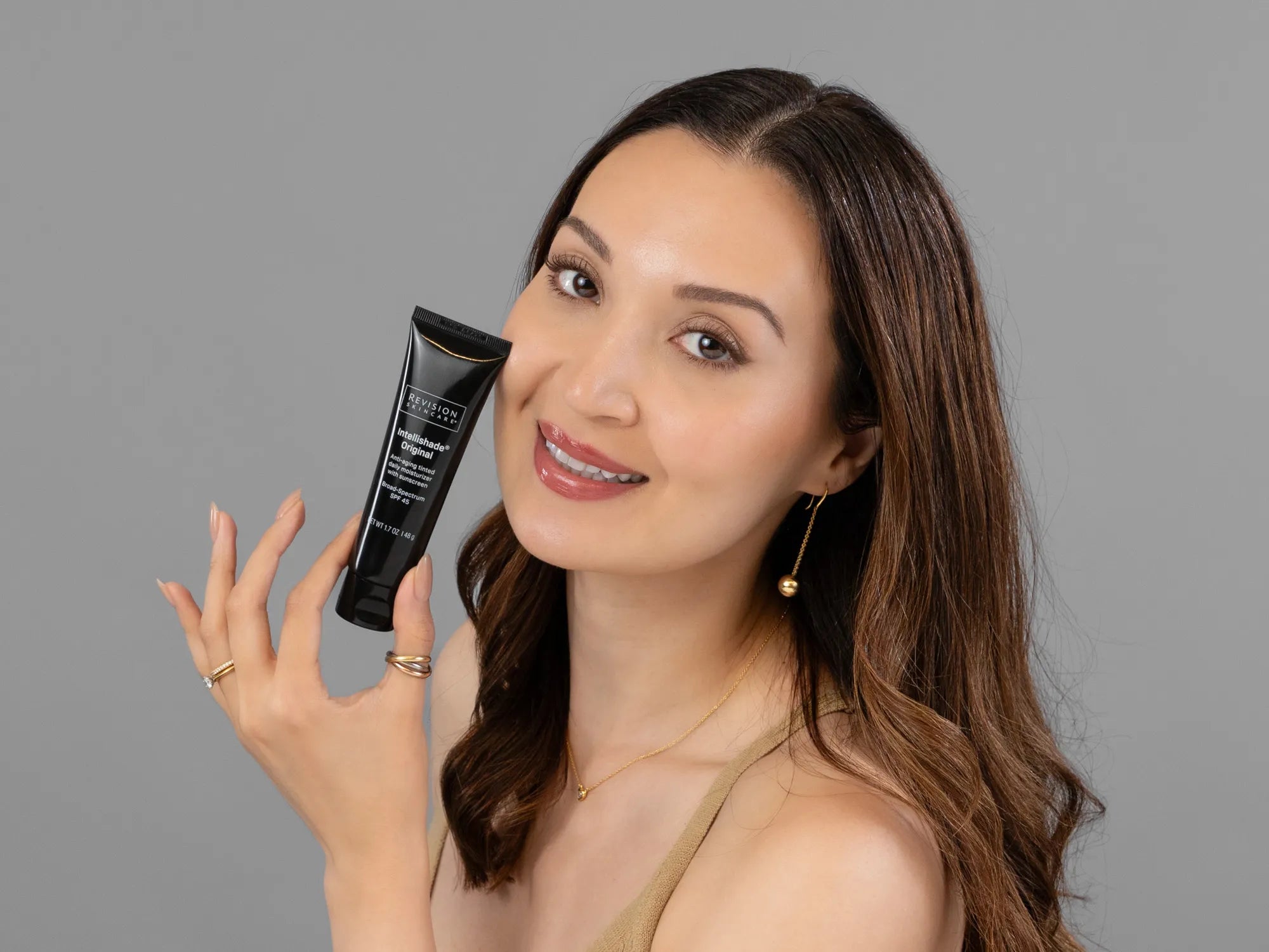 Laziza from LAZ Skincare holding a bottle of Revision Intellishade Original SPF 45 up to her face