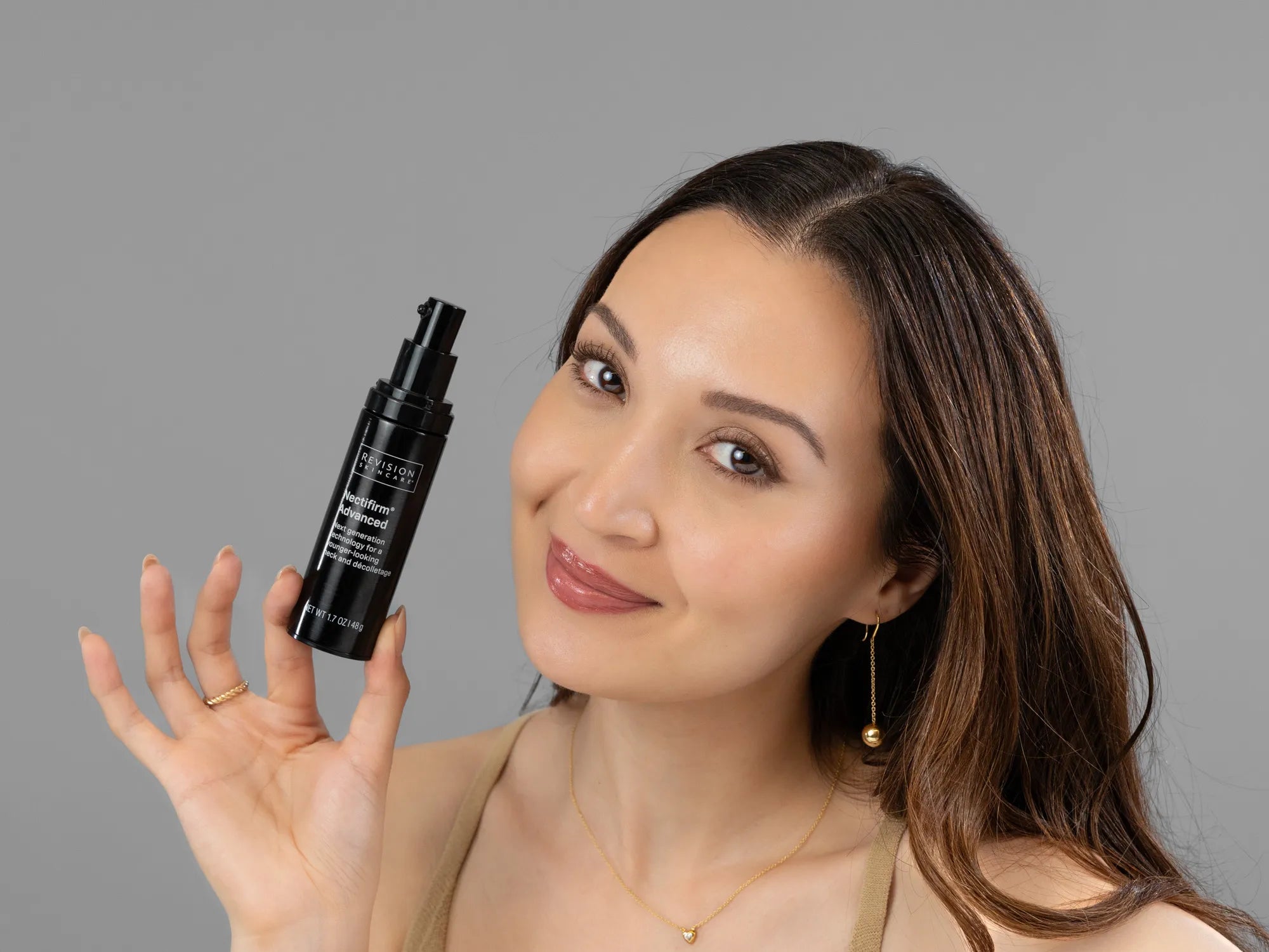 Laziza from LAZ Skincare holding a bottle of Revision Nectifirm Advanced up to her face
