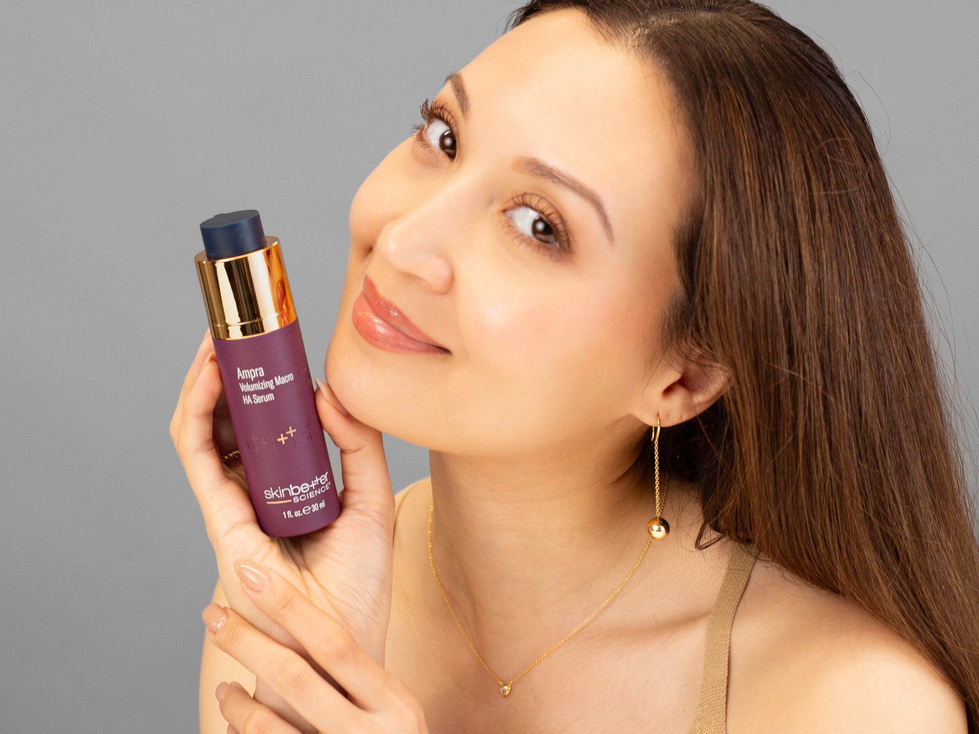 Laziza from LAZ Skincare holding a bottle of SkinBetter Science Ampra Volumizing Serum up to her face