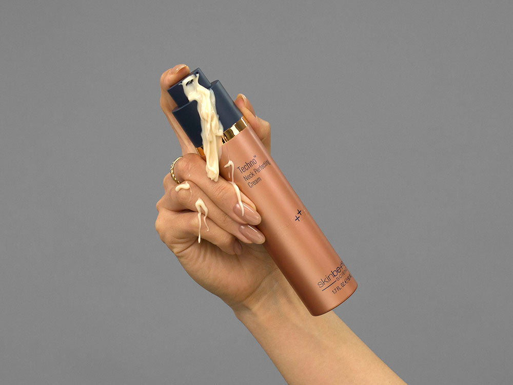 Closeup of Laziza from LAZ Skincare holding up a bottle of SkinBetter Science Techno Neck Perfecting Cream