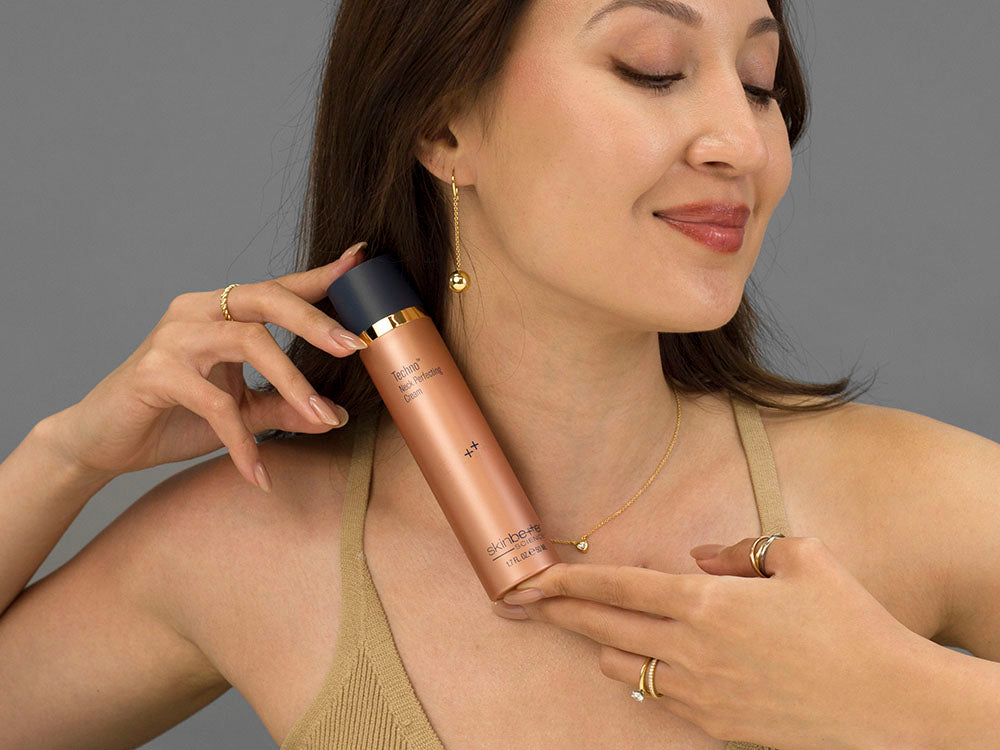 Laziza from LAZ Skincare holding a bottle of SkinBetter Science Techno Neck Perfecting Cream up to her face