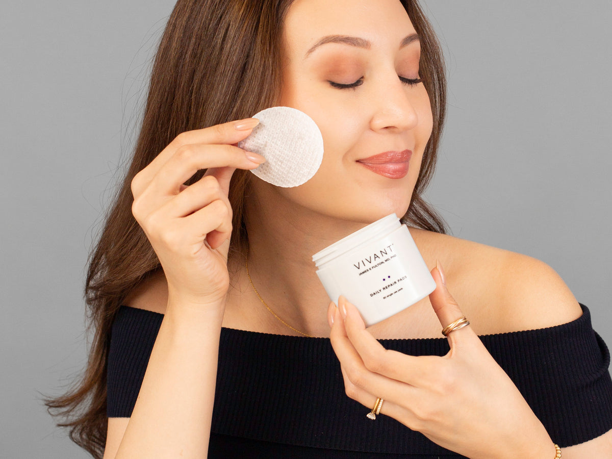 Laziza from LAZ Skincare holding a bottle of Vivant Daily Repair Pads up to her face