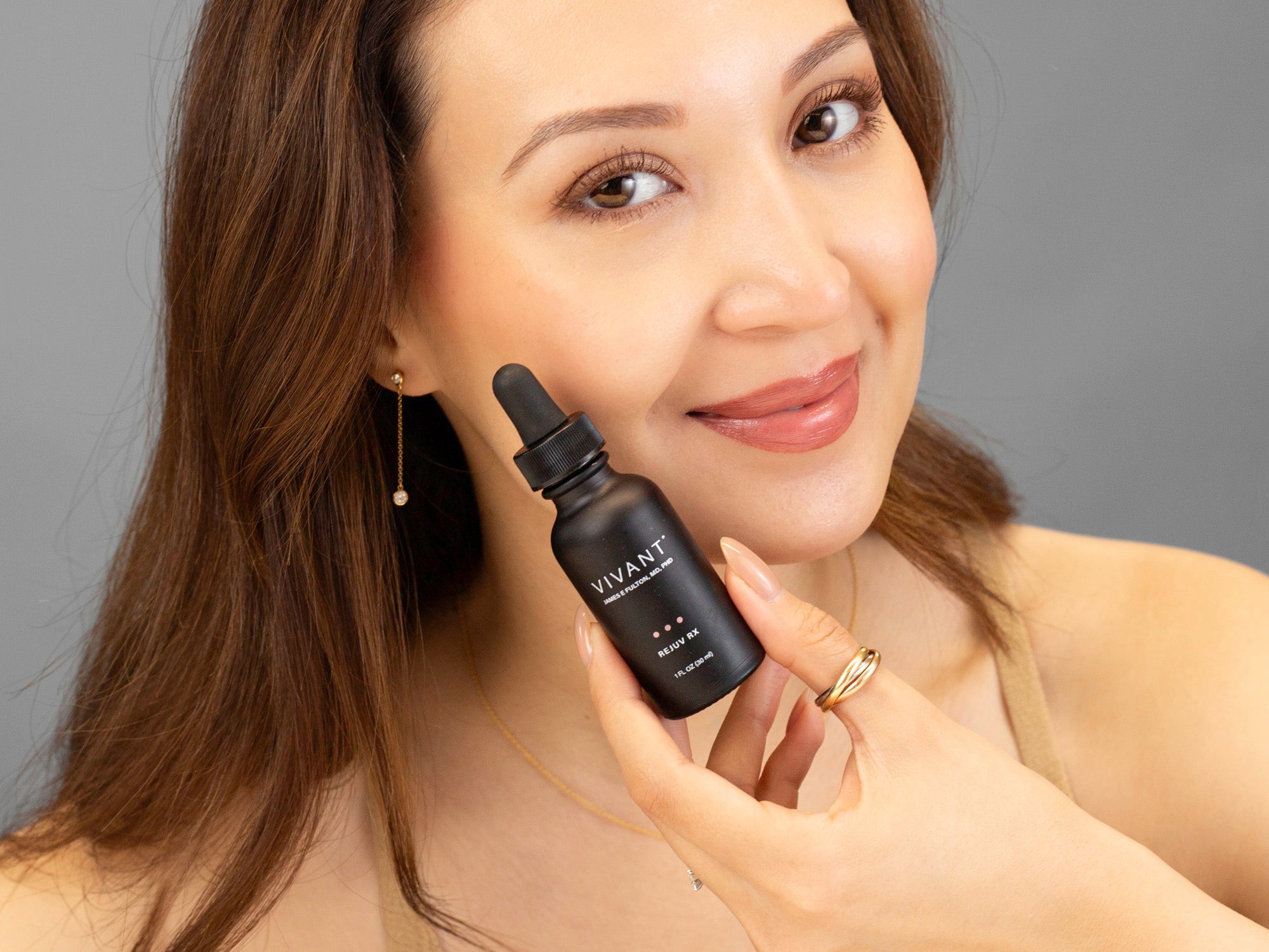 Laziza from LAZ Skincare holding a bottle of Vivant Rejuv Rx up to her face