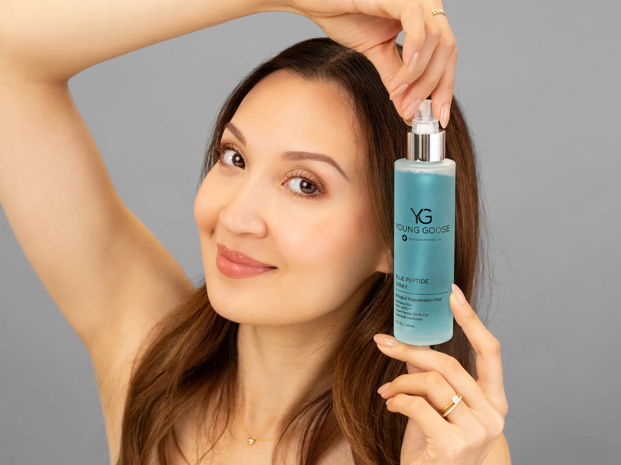 Laziza from LAZ Skincare holding a bottle of Young Goose Blue Peptide Spray up to her face