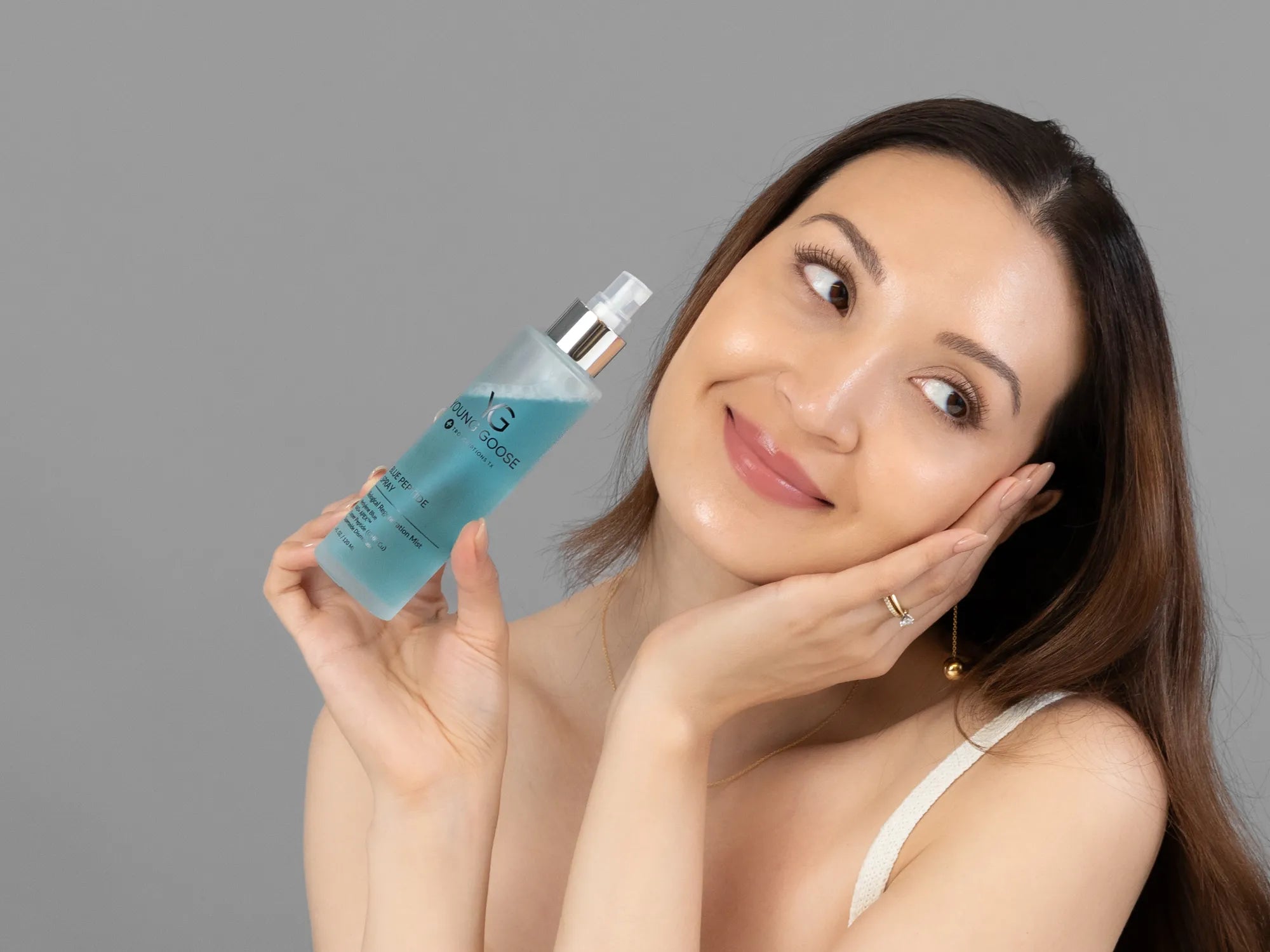 Laziza from LAZ Skincare holding a bottle of Young Goose Blue Peptide Spray up to her face