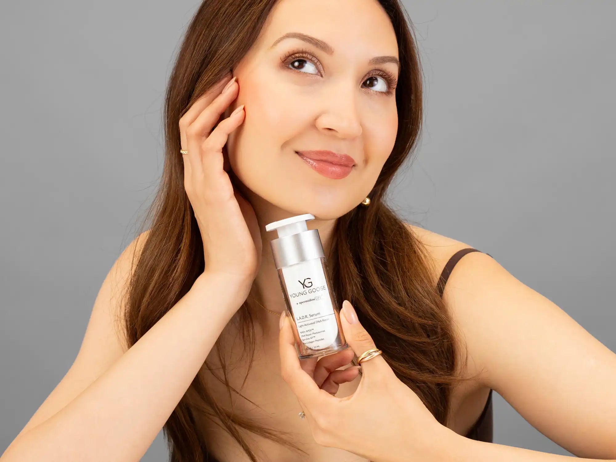 Laziza from LAZ Skincare holding a bottle of Young Goose L.A.D.R. Serum up to her face