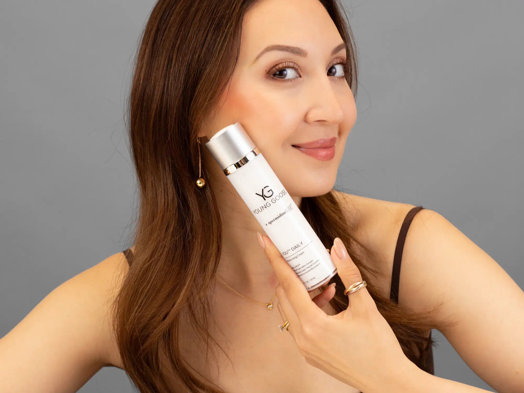 Laziza from LAZ Skincare holding a bottle of Young Goose Youth Daily up to her face