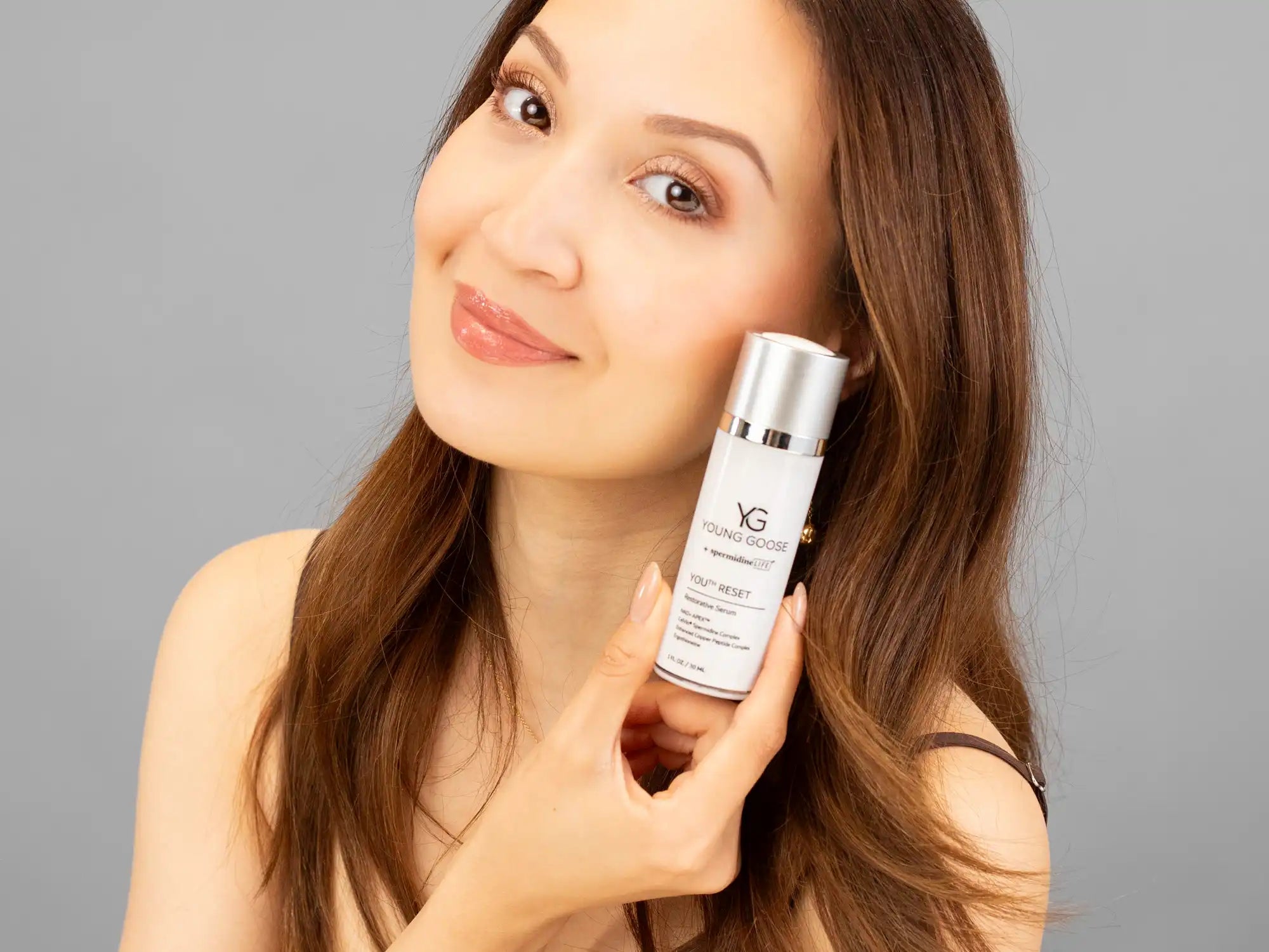 Laziza from LAZ Skincare holding a bottle of Young Goose Youth Reset up to her face