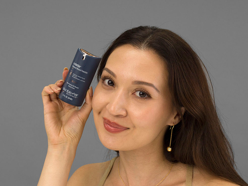 Laziza from LAZ Skincare holding a bottle of SkinBetter Science sunbetter TONE SMART SPF 75 Sunscreen Lotion up to her face